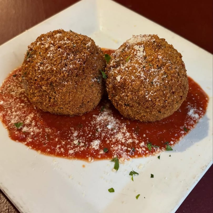Two golden-brown arancini balls, sprinkled with parmesan, resting in a pool of marinara sauce.
