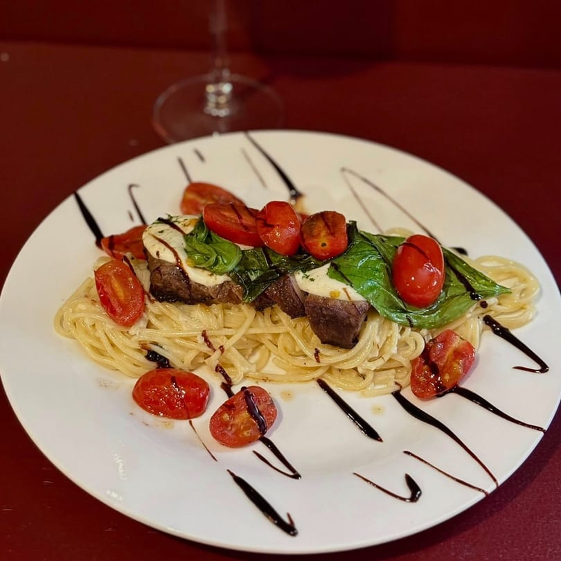 Spaghetti with steak, mozzarella, basil, cherry tomatoes, and balsamic glaze on a white plate.