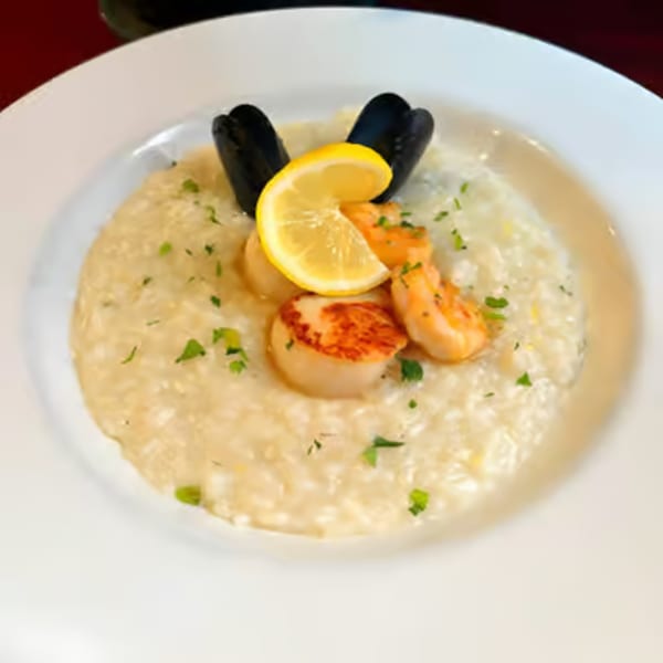 Creamy seafood risotto with mussels, shrimp, scallops, parsley, and a lemon slice in a white bowl.