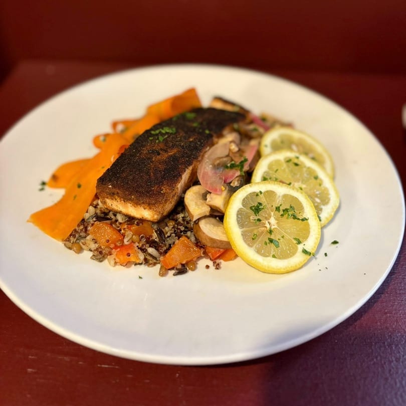 Blackened salmon with wild rice, butternut squash, mushrooms, and lemon slices on a white plate.